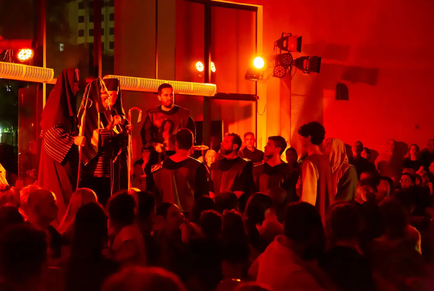 The trial scene under a deep red wash, stage fixtures visible above the crowd