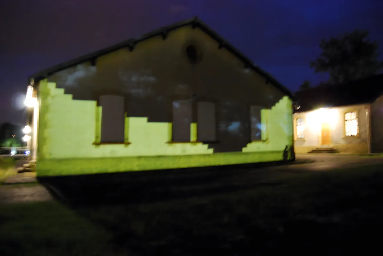 The barrack facade under projected light, a lit hall glowing behind
