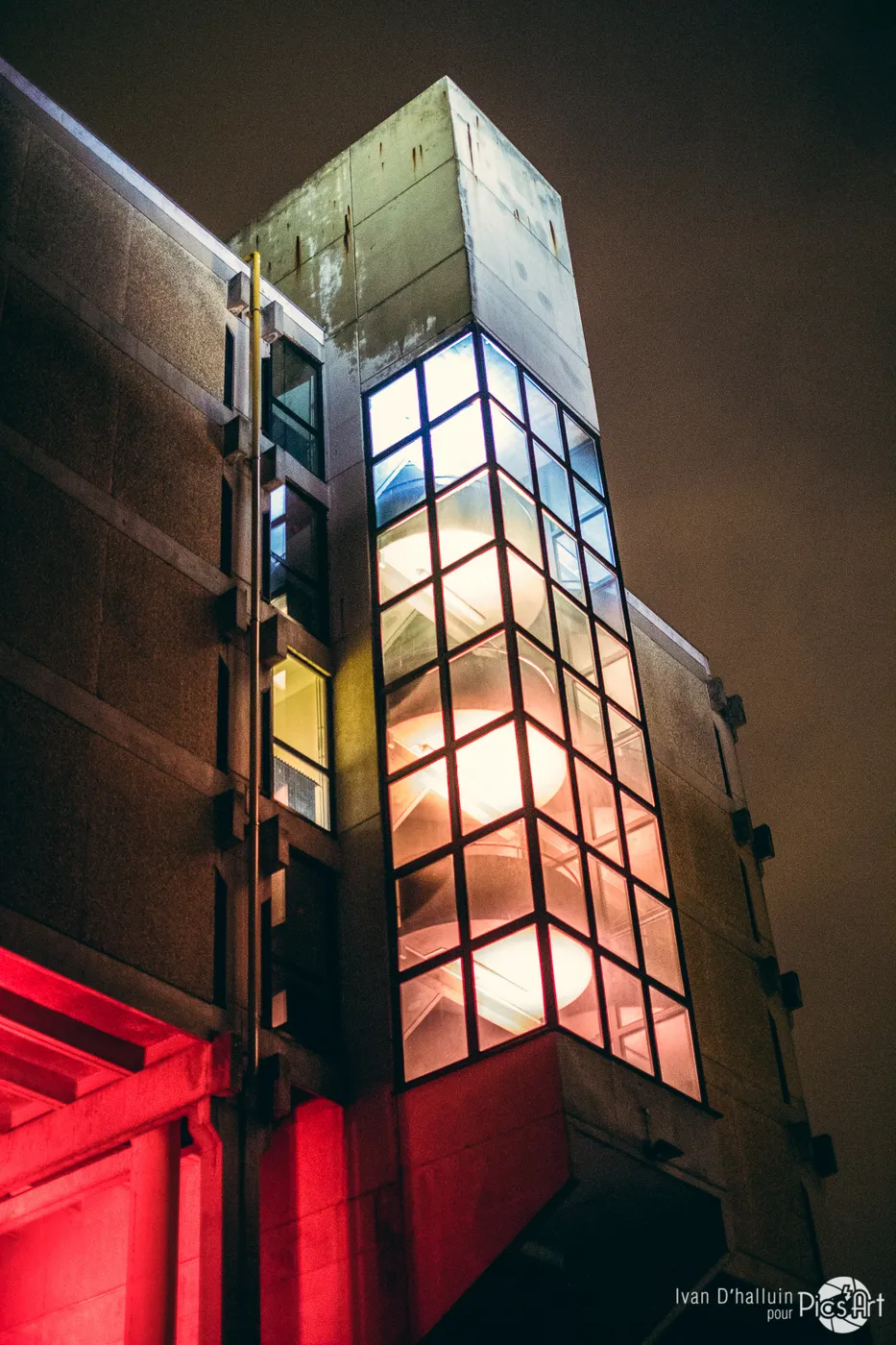 A glass stairwell tower glowing warm white against the night