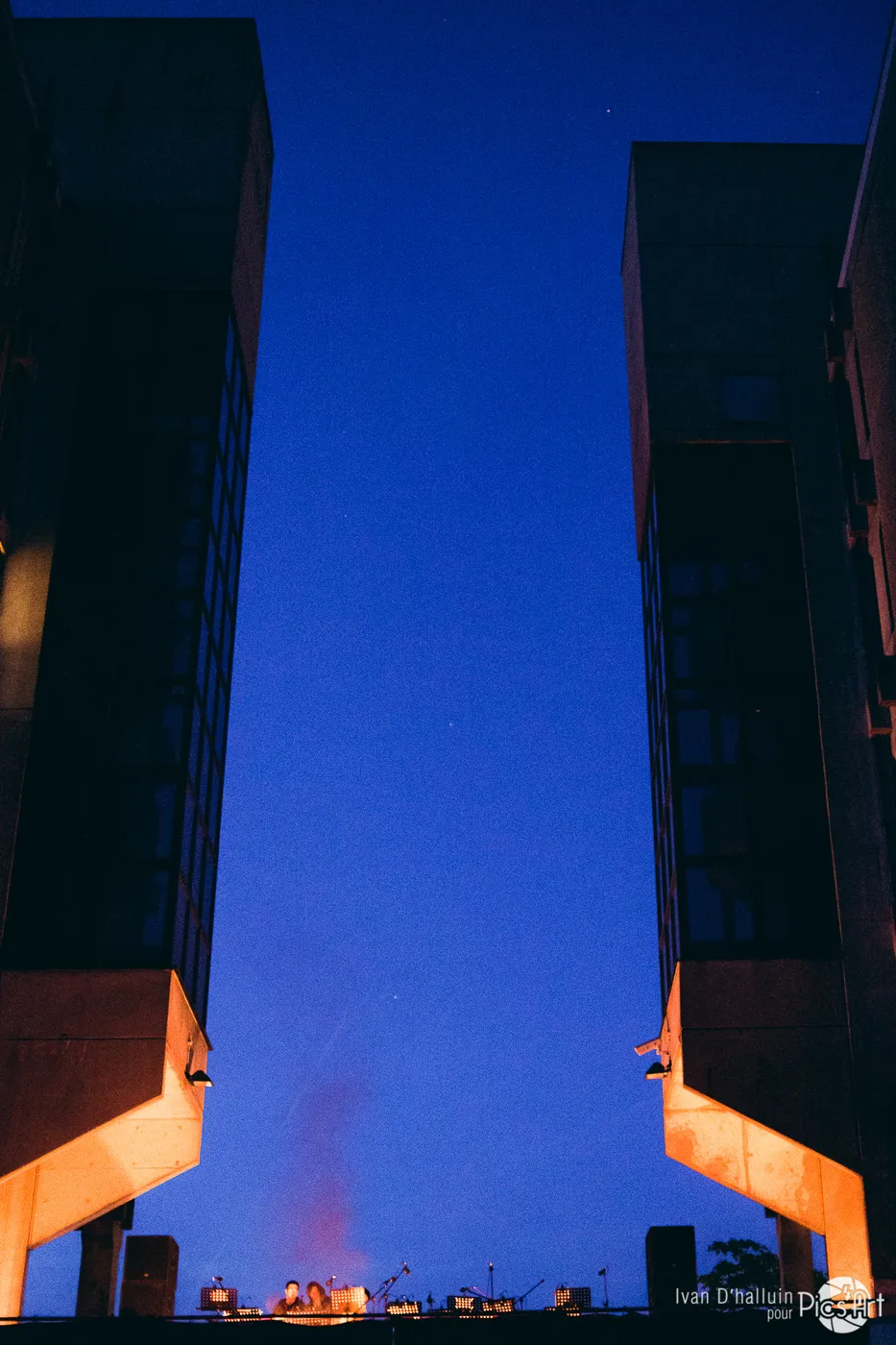 Two towers framing a deep-blue twilight, a small stage glowing below